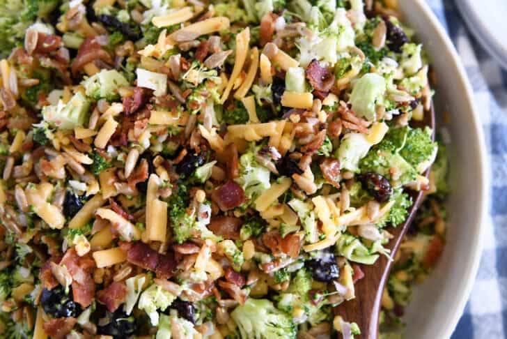 Top down view of chopped broccoli salad with shredded cheese, diced onion, bacon bits, sunflower seeds, and dried cranberries coated in a light sauce.