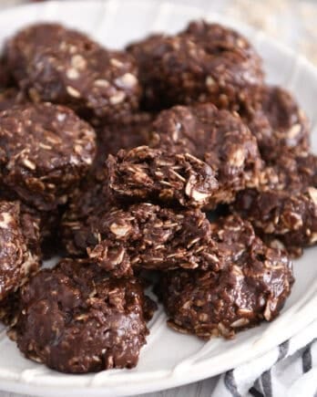 Stack of chocolate no-bake cookies on white plate with one cookie broken in half.
