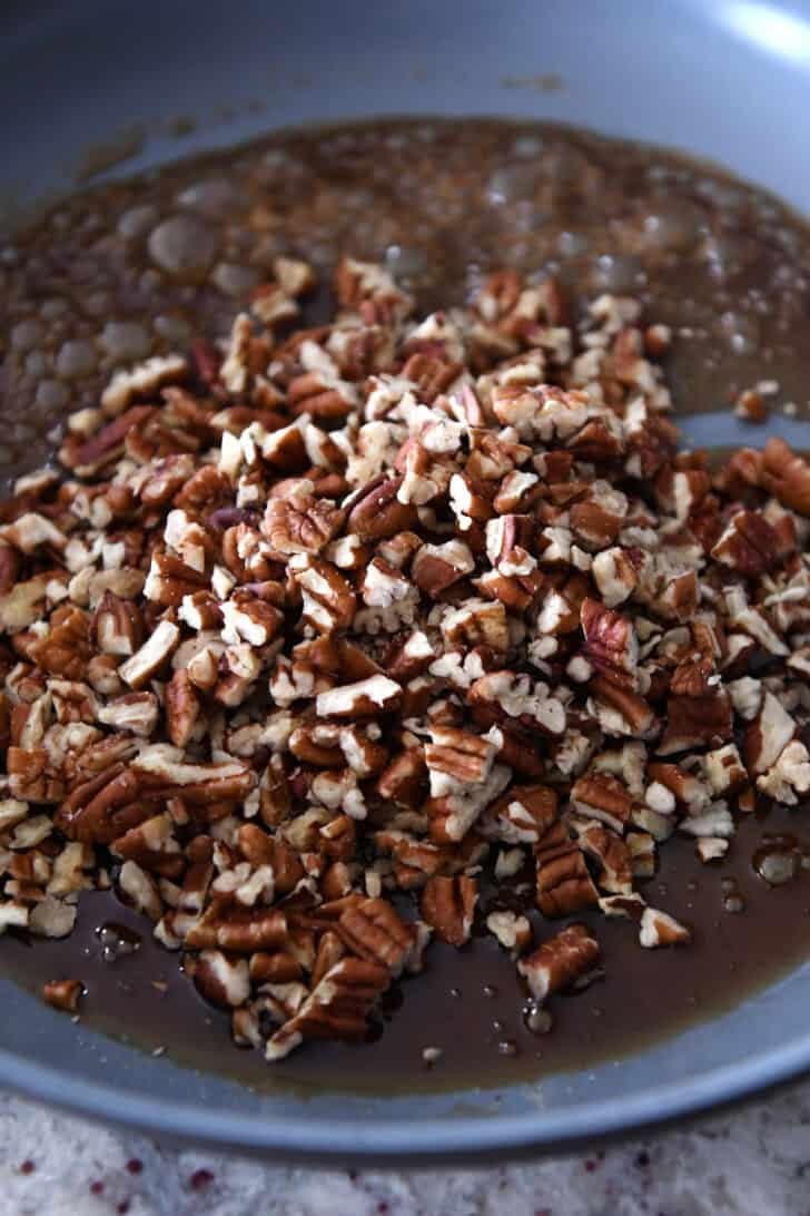 A melted syrup and chopped pecans in a metal skillet.