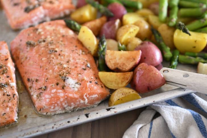 Sheet pan with baked piece of lemon garlic salmon, roasted potatoes and asparagus.