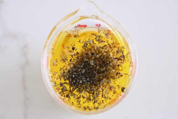 Liquid measuring cup of olive oil, lemon juice, garlic, oregano and basil.