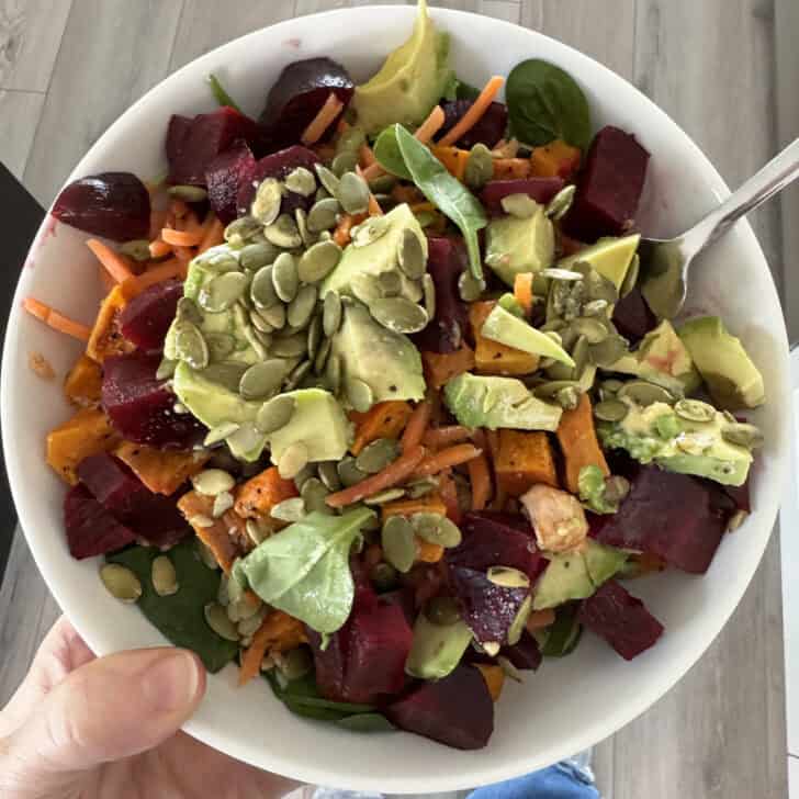 White bowl with beets, sweet potatoes, avocados, pumpkin seeds, spinach and tuna.
