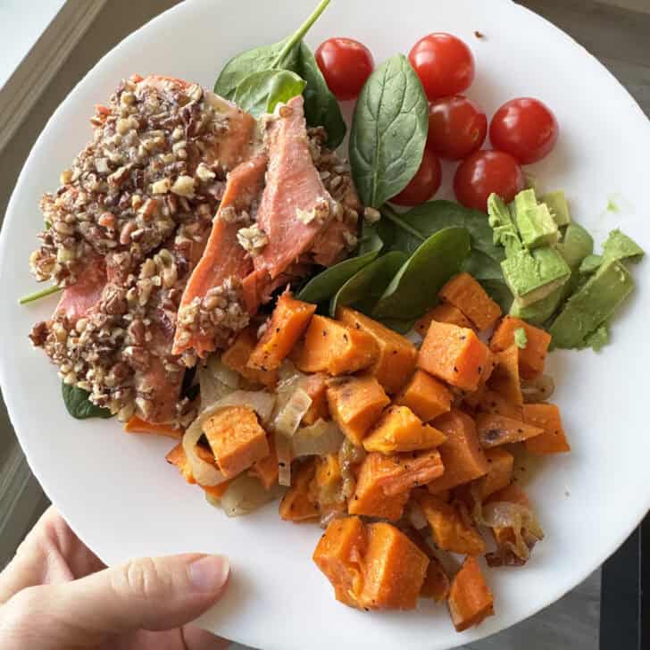 White plate with salmon, sweet potatoes, spinach, avocados, and cherry tomatoes.