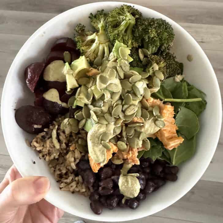 White bowl with beets, pumpkin seeds, tuna, spinach, broccoli, black beans and brown rice.