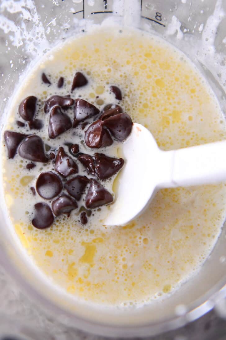Top down view of a rubber spatula stirring melted chocolate chips into melted butter in a measuring cup.