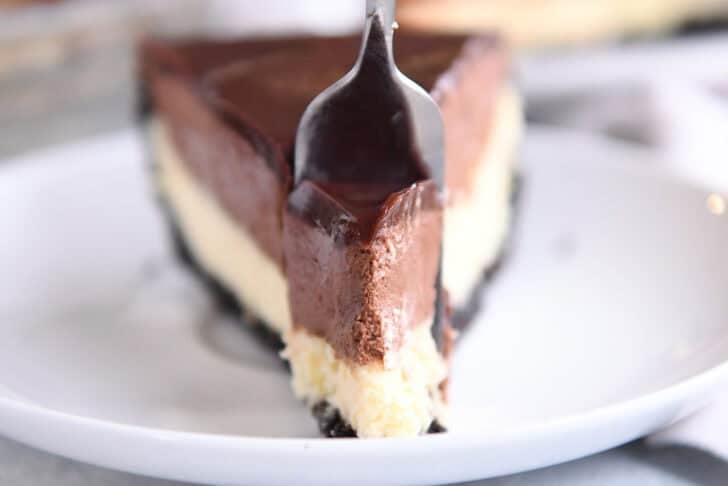 A fork taking a bite out of a slice of chocolate mousse cheesecake.
