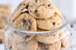 Glass jar filled with mini chocolate chip cookies with mini chocolate chips around bottom.