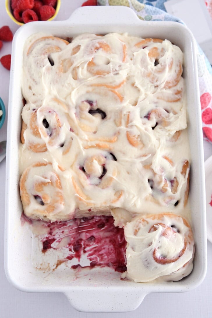 White 9X13-inch pan of baked raspberry sweet rolls spread with sweet cream cheese icing.