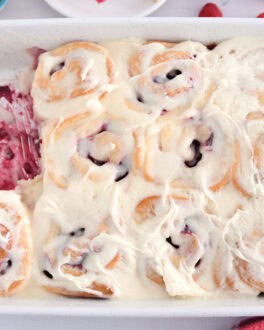 White 9X13-inch pan of baked raspberry sweet rolls spread with sweet cream cheese icing.
