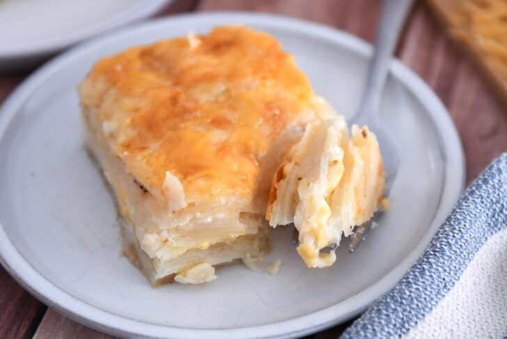 Square of baked au gratin potatoes on gray plate with fork taking piece from corner.
