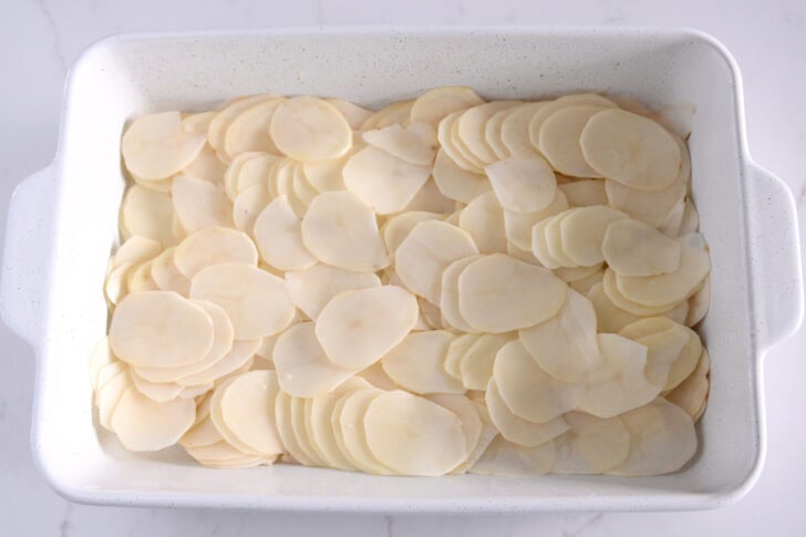 White 9X13-inch dish layered with thin potatoes.