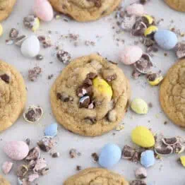 Baked cookies on parchment paper with crushed and whole cadbury eggs scattered around.