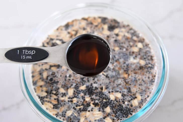 Pouring tablespoon of pure maple syrup into overnight chia oats.