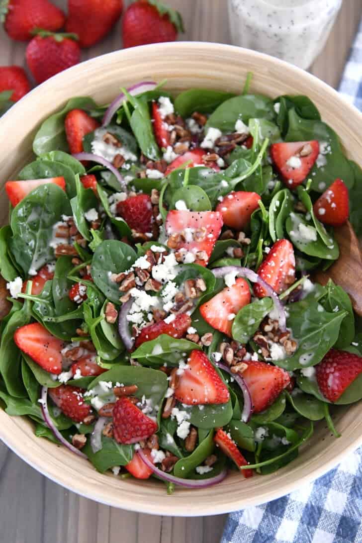 Wooden salad bowl with fresh spinach, sliced strawberries, sliced red onions, feta cheese, chopped pecans and poppy seed dressing.
