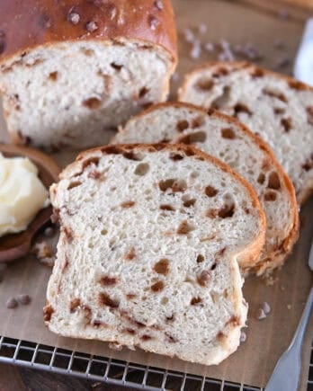 Slice of cinnamon burst bread on brown parchment paper with butter on wooden dish to the side.