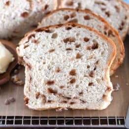 Slice of cinnamon burst bread on brown parchment paper with butter on wooden dish to the side.