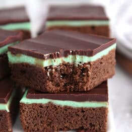 White tray of squares of chocolate mint brownies with top brownie with bite taken out.