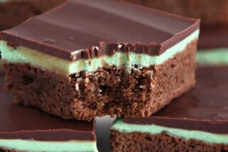 White tray of squares of chocolate mint brownies with top brownie with bite taken out.