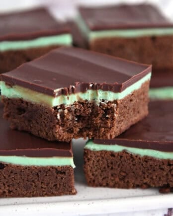 White tray of squares of chocolate mint brownies with top brownie with bite taken out.