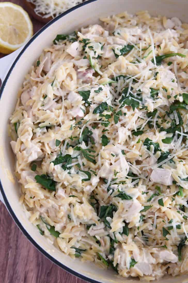 Top down view of cooked creamy lemon orzo in white pan with spinach and chicken.