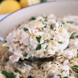 Serving spoon with scoop of creamy orzo, spinach and chicken.