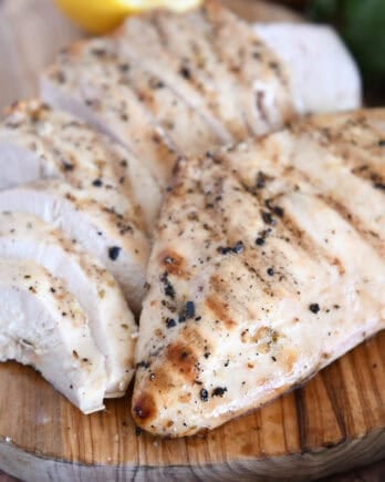 Grilled chicken breast on wood platter with sliced chicken.