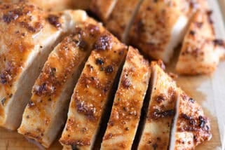 Sliced cooked chicken breasts on wood cutting board.