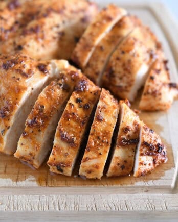Sliced cooked chicken breasts on wood cutting board.