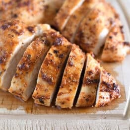 Sliced cooked chicken breasts on wood cutting board.