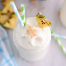Top down view of tall glass cup with frozen piña colada, toasted coconut, a triangle of fresh pineapple and a bit of toasted coconut on top.