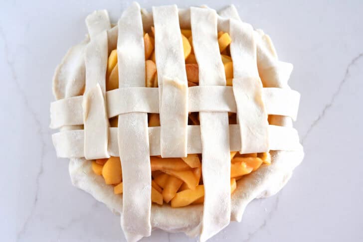 Assembling lattice pie crust on fresh peach pie.
