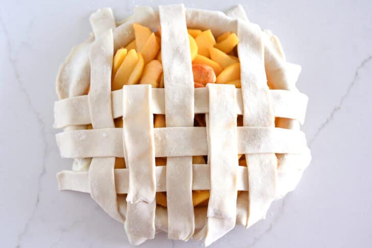 Assembling lattice pie crust on fresh peach pie.
