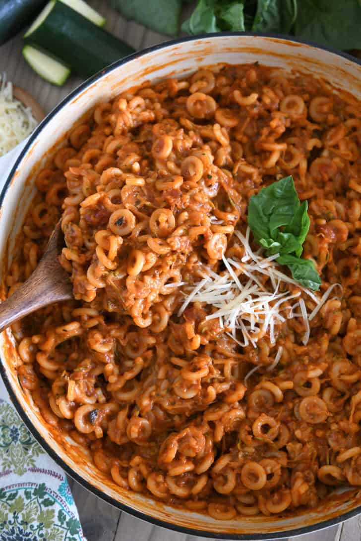 Serving spoon scooping up helping of saucy pasta out of deep skillet.