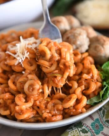 Saucy pasta with shredded zucchini piled high on plate with fork scooping bite.