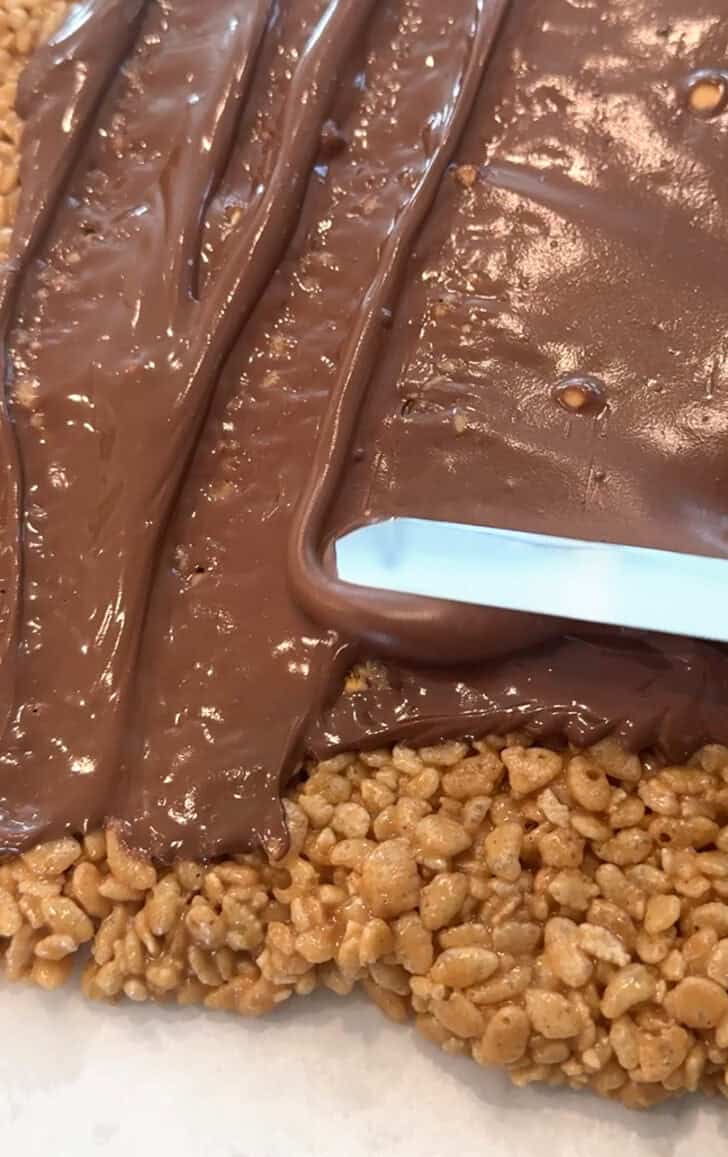 Spreading chocolate onto scotcheroo mixture.