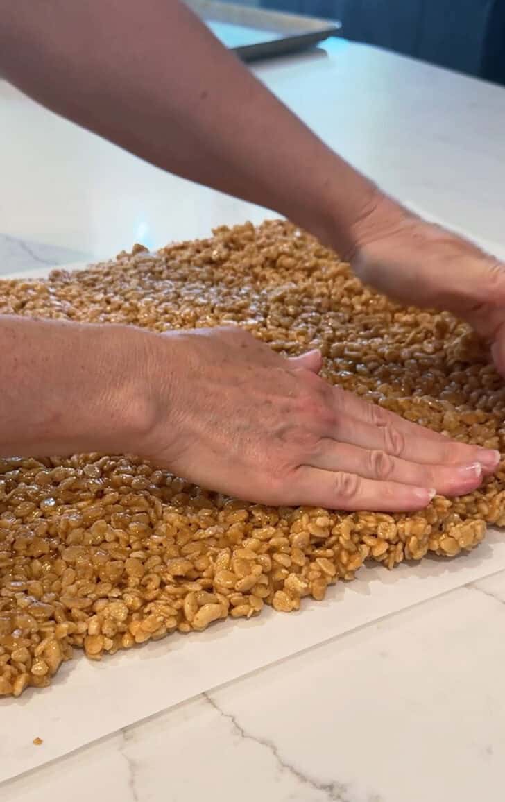 Pressing scotcheroos into thin layer on parchment paper.