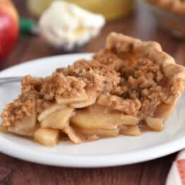 Slice of apple crumble pie on white plate with fork.