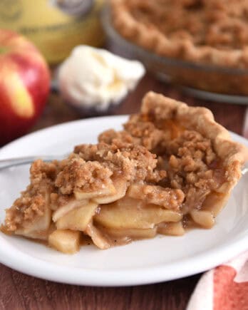 Slice of apple crumble pie on white plate with fork.