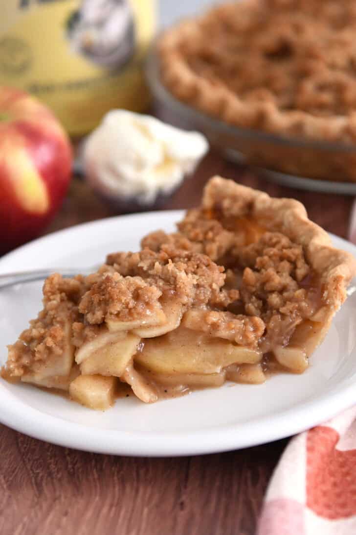 Slice of apple crumble pie on white plate with fork.