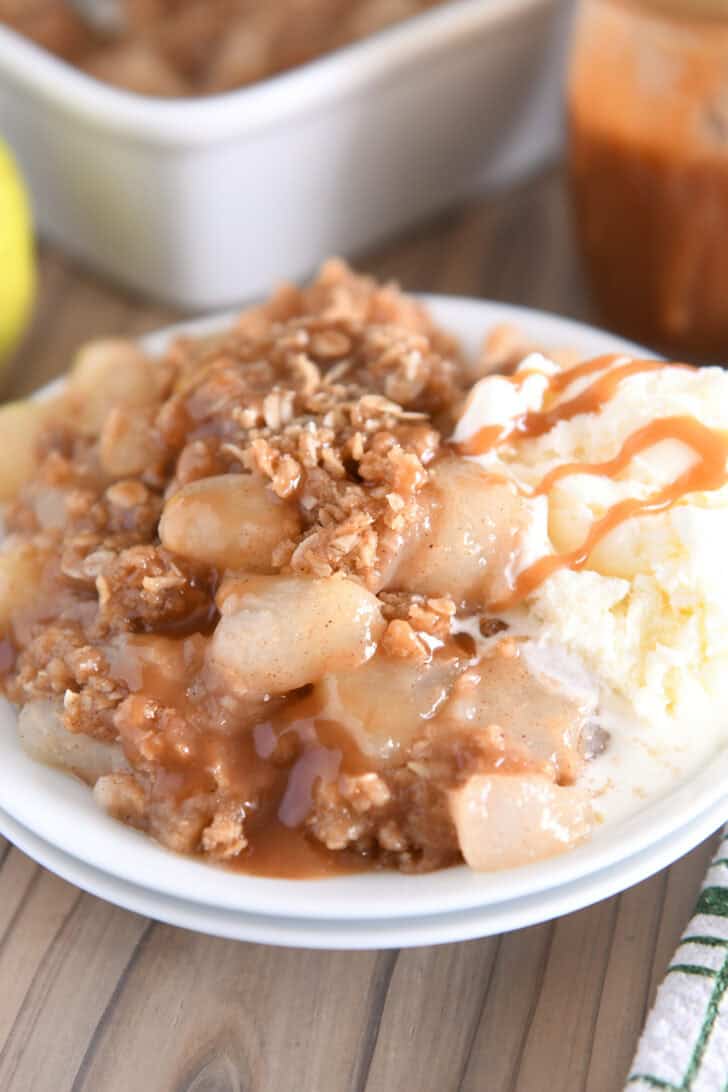 Double stack of white plates with serving of caramel pear crisp and vanilla ice cream.
