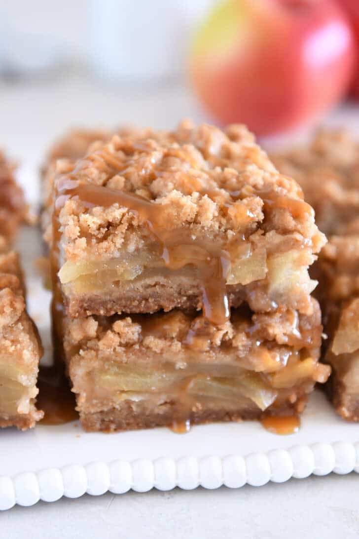 Two caramel apple crumble bars stacked on white tray.