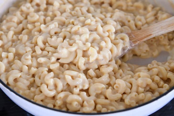 Scooping creamy skillet macaroni and cheese in white cast iron skillet with wooden spoon.