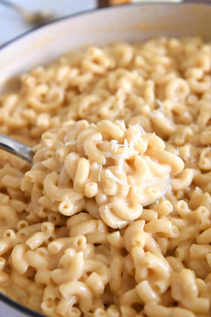 Serving spoon scooping creamy skillet macaroni and cheese.