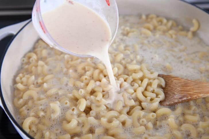 Pouring evaporated milk, cornstarch, hot sauce and dry mustard into skillet mac and cheese.