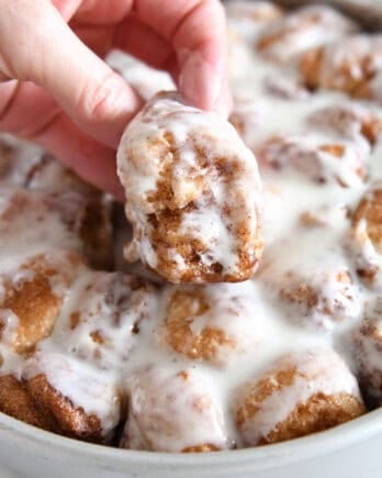 Lifting fluffy cinnamon roll bite out of pan of cinnamon roll bites.