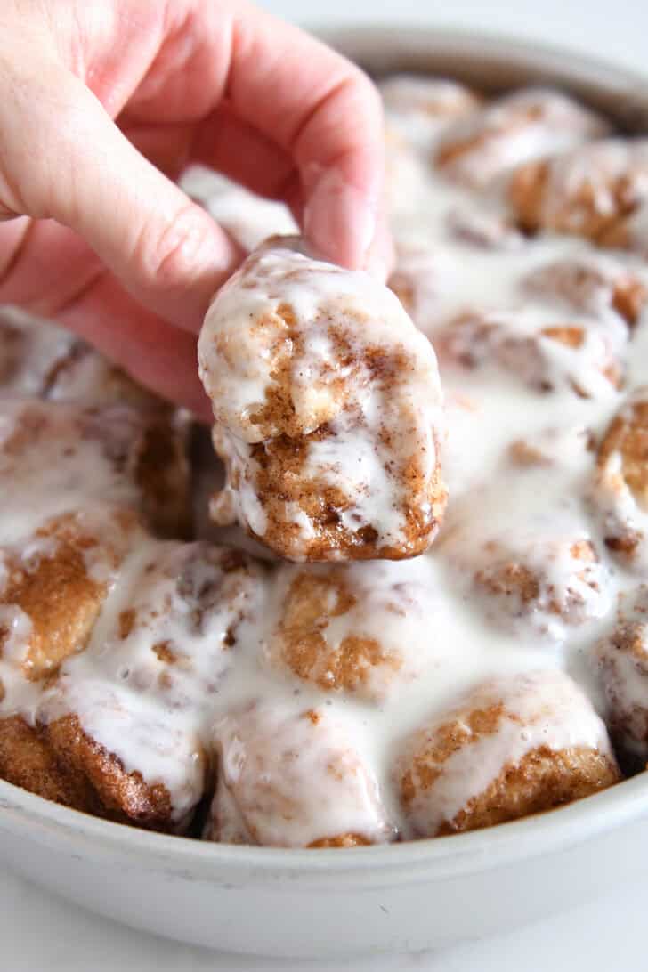 Lifting fluffy cinnamon roll bite out of pan of cinnamon roll bites.