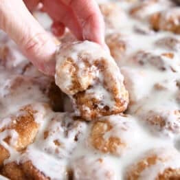 Lifting fluffy cinnamon roll bite out of pan of cinnamon roll bites.
