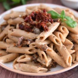 Brown rimmed plate with cooked Instant Pot marry. me pasta with sun-dried tomatoes on top with fresh basil.