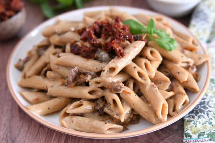 Brown rimmed plate with cooked Instant Pot marry. me pasta with sun-dried tomatoes on top with fresh basil.