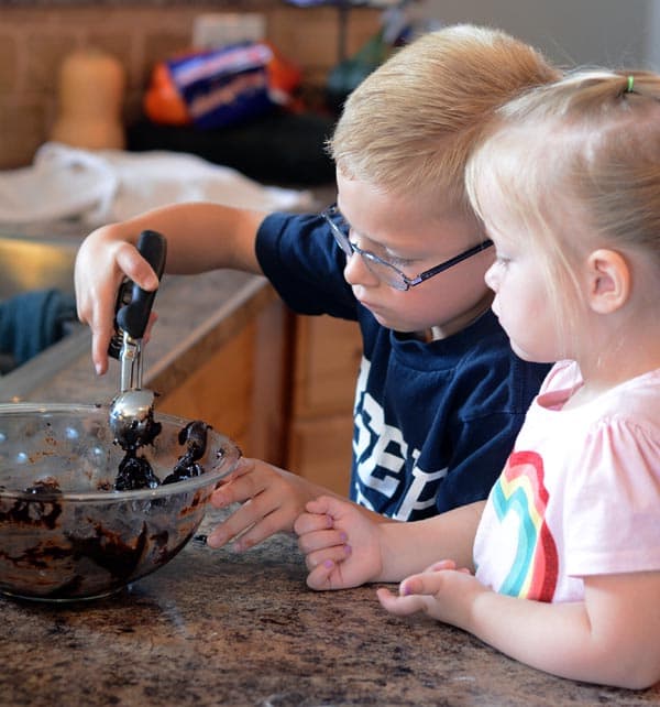 A little girl and boy scooping cookie dough together. 